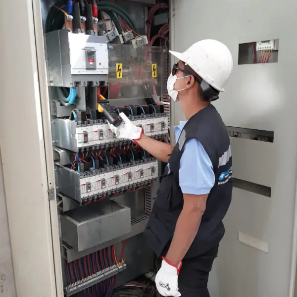 Técnico inspeccionando un tablero eléctrico con multímetro, usando equipo de protección.