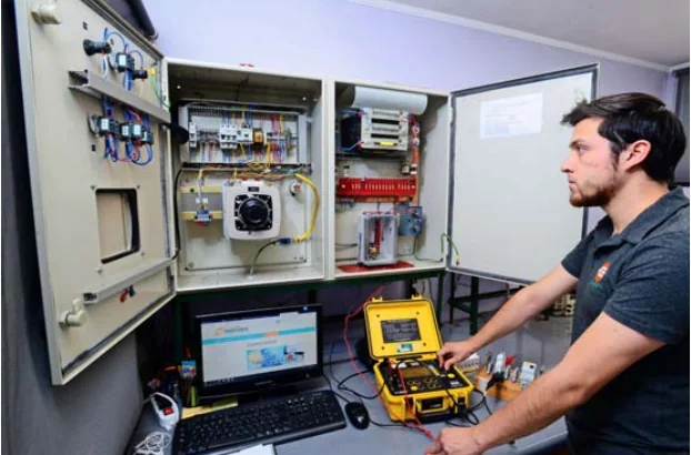 Técnico usando analizador portátil frente a gabinetes abiertos y computador para verificar protecciones, continuidad y puesta a tierra durante la instalación de tableros