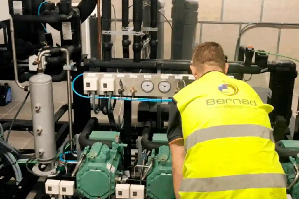 Técnico con chaleco revisa central de compresores y manómetros durante el mantenimiento preventivo a equipos de refrigeración industrial