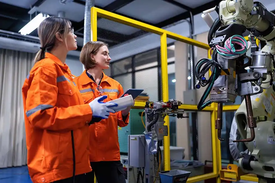 Técnicas de mantenimiento integral aplicado a maquinaria industrial, con ingenieras realizando inspección y ajustes a un robot automatizado en un entorno de fábrica.