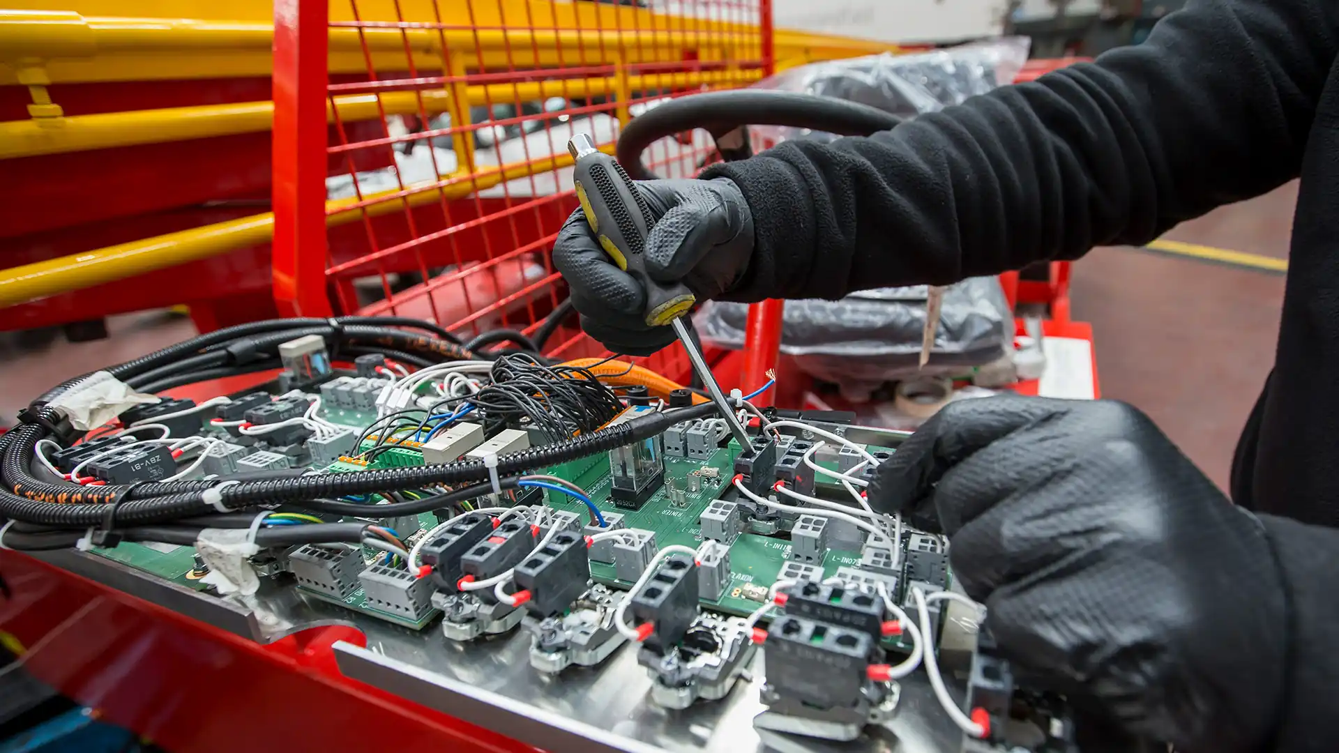 Técnico realizando mantenimiento integral en un sistema electrónico industrial, con atención en la instalación de cables y componentes eléctricos en una placa de circuito, asegurando el funcionamiento óptimo de los equipos.