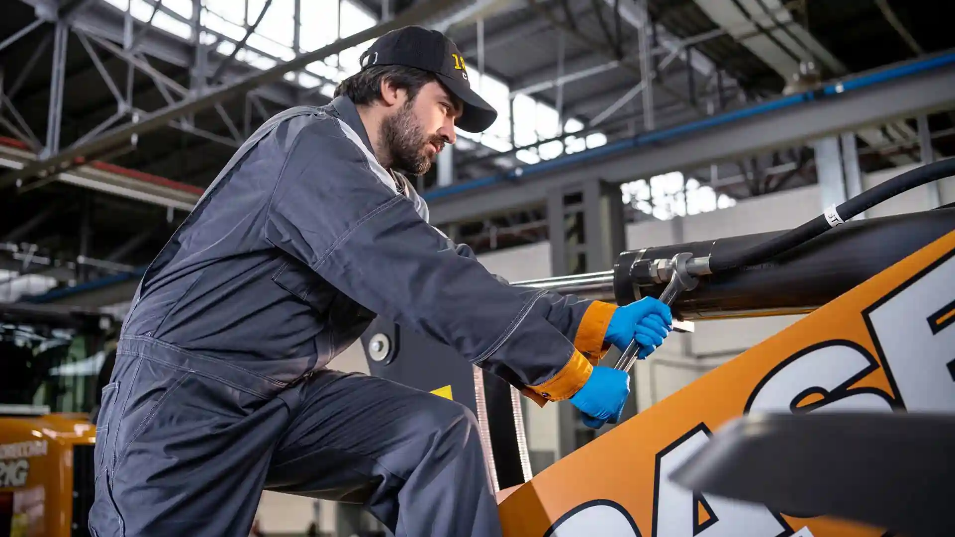 Técnico con overol y guantes ajusta conexiones del cilindro hidráulico durante el mantenimiento preventivo de cargador frontal, asegurando estanqueidad y rendimiento continuo en faena.