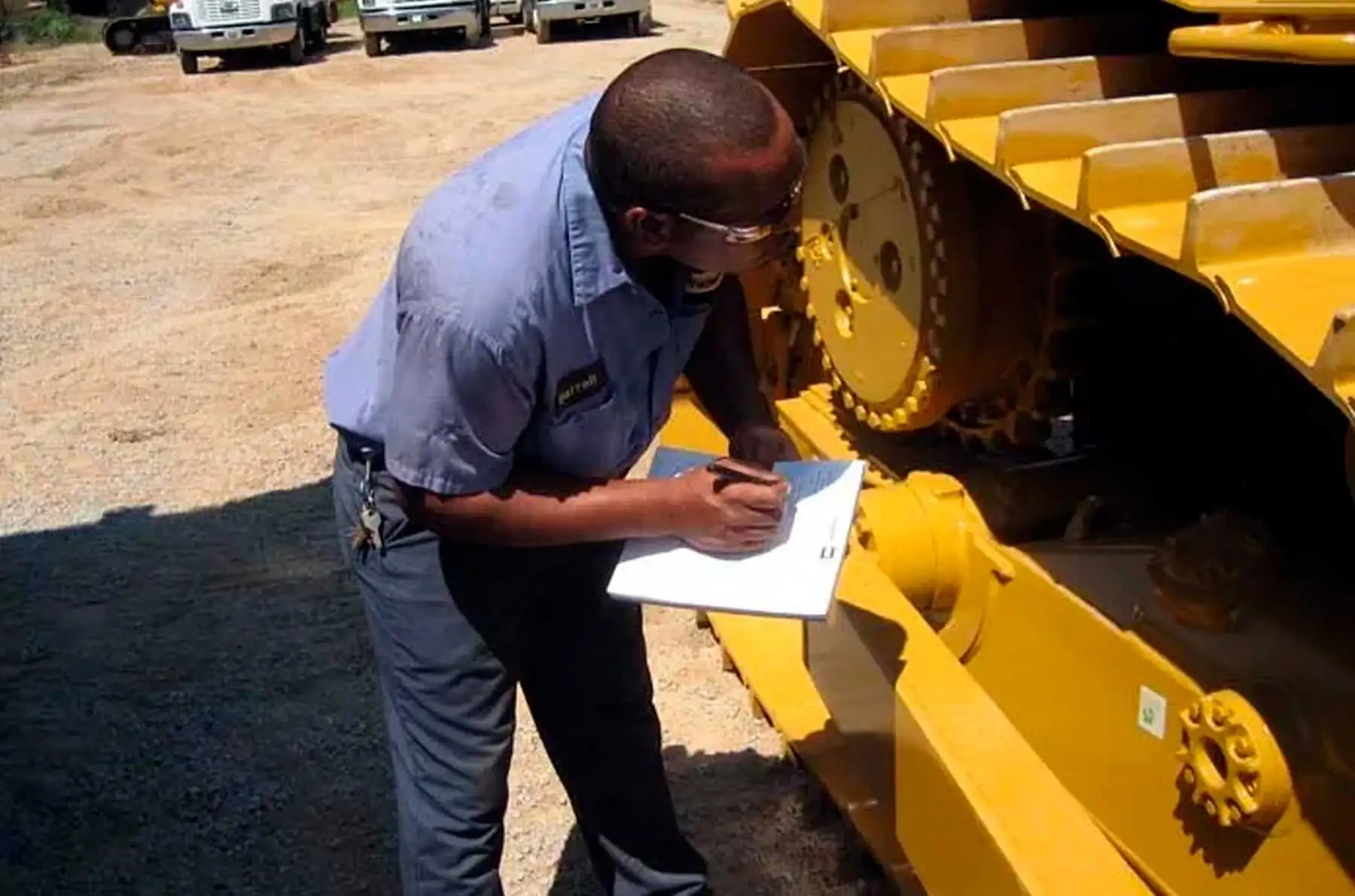 Técnico con portapapeles registra checklist junto al tren de rodaje de equipo oruga durante el mantenimiento preventivo de maquinaria