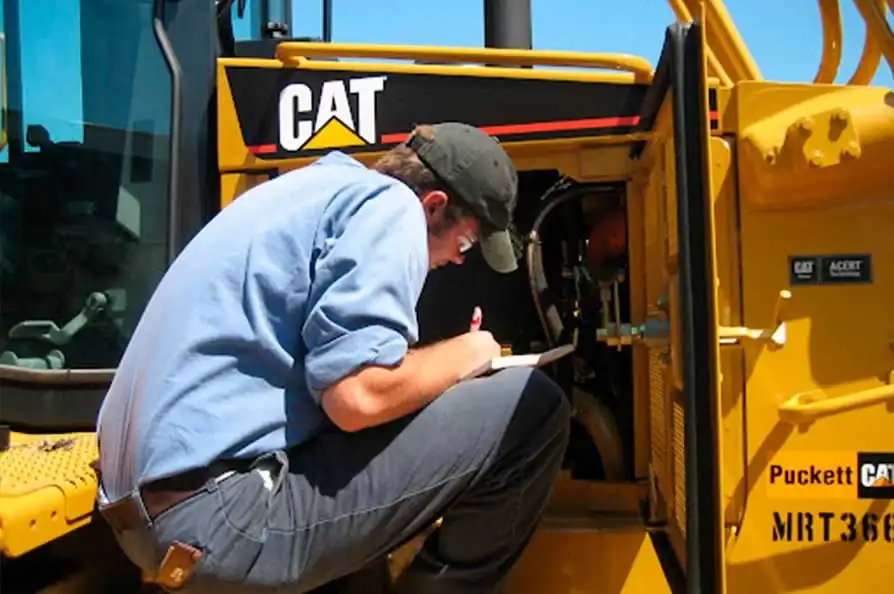 Técnico con clipboard revisa el compartimiento del motor de maquinaria pesada CAT durante el mantenimiento preventivo de maquinaria
